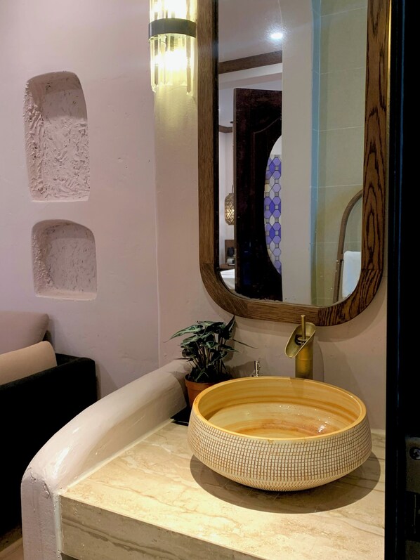 A bathroom with a round sink, a mirror, and a wall-mounted light fixture.