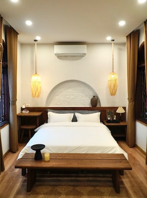 A hotel room with a large bed, bedside tables, a bench, an air conditioning unit, and two hanging lamps. - The General's House - Garden Villa (Hoan Kiem)