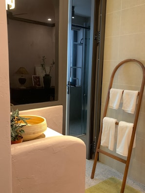 A bathroom with a glass shower door, a wooden towel rack, and a potted plant on the counter. - The General's House - Garden Villa (Hoan Kiem)