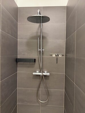 Suihkussa on käsisuihkupää, seinään kiinnitetty ohjauspaneeli ja käsisuihkuletku.