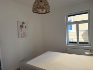 A bedroom with a single bed, a window with blinds, a wall-mounted light fixture, and a painting. - Modern City Apartment at Sendlinger Tor – 5 minutes from downtown – right in the heart of Munich (München)