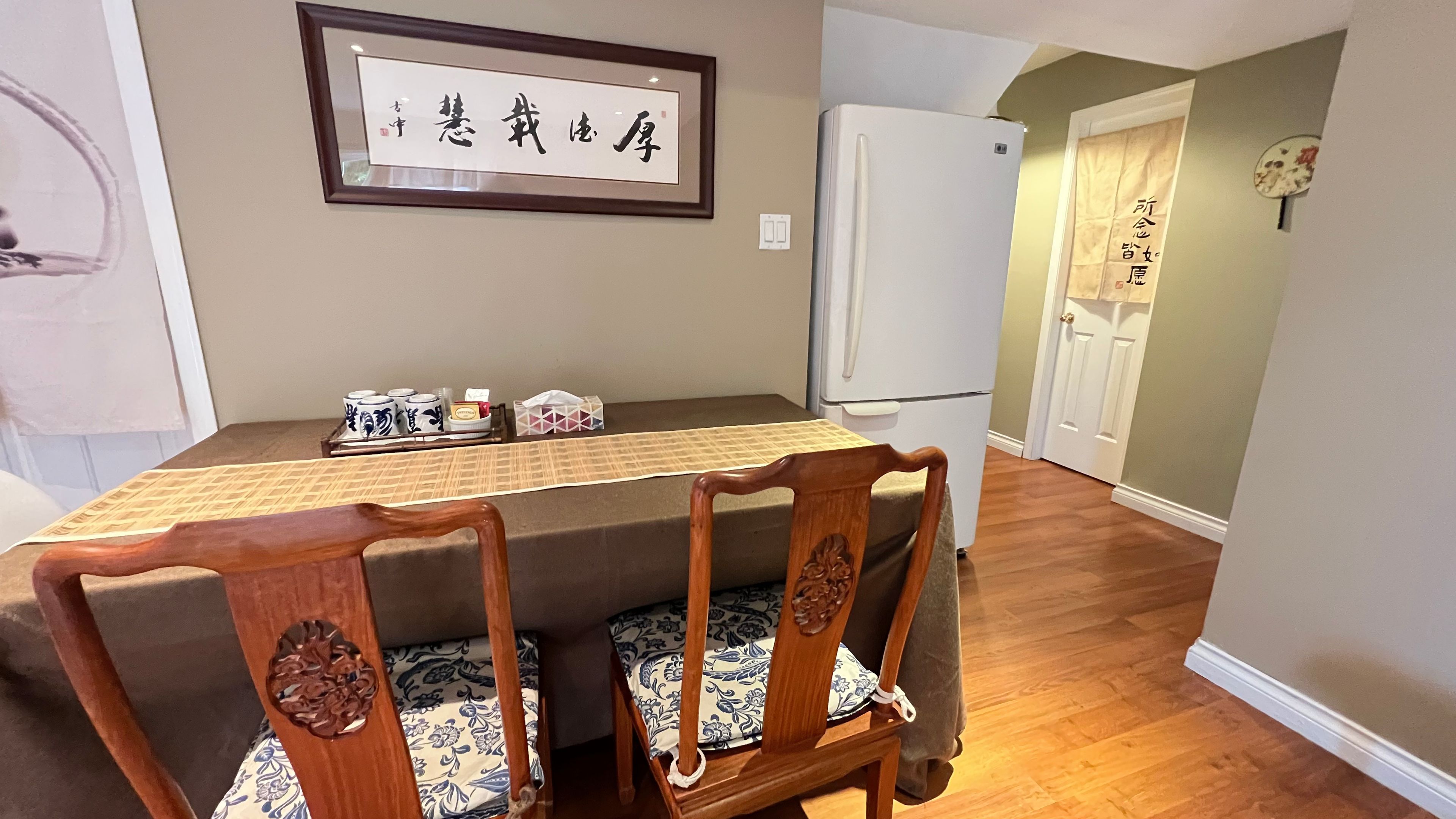 A dining area with a table, chairs, a refrigerator, and a framed sign on the wall.