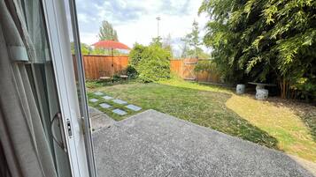 Un patio trasero con cerco de madera, una sombrilla roja y un área de patio empedrado.