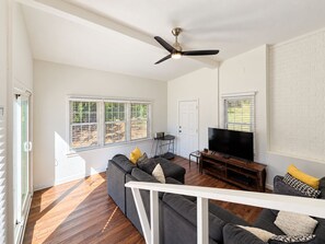 Un salon spacieux doté d’un ventilateur de plafond, d’un grand téléviseur à écran plat et d’un ensemble de canapés.