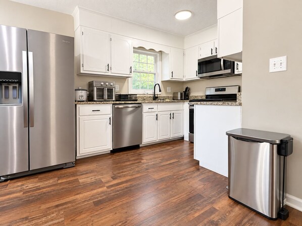 A modern kitchen with stainless steel appliances, white cabinetry, and a herringbone wood floor. - Cozy 3-bedroom Rocky Mount Home Retreat With Full Kitchen & Fenced Yard (Rocky Mount)