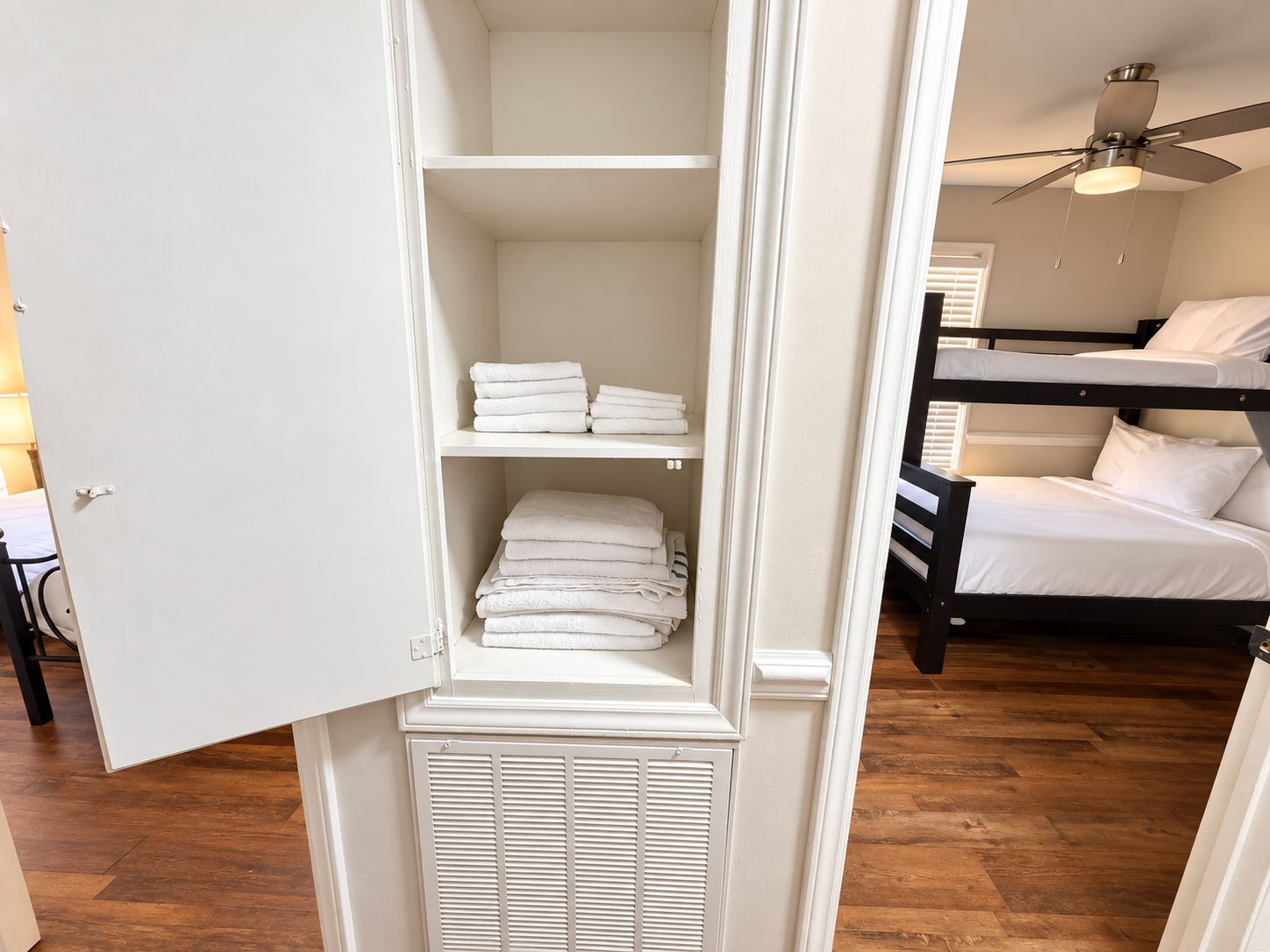 Una habitación con literas, un armario blanco con estantes y un ventilador de techo.
