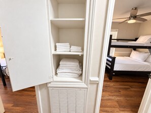 Una habitación con literas, un armario blanco con estantes y un ventilador de techo.