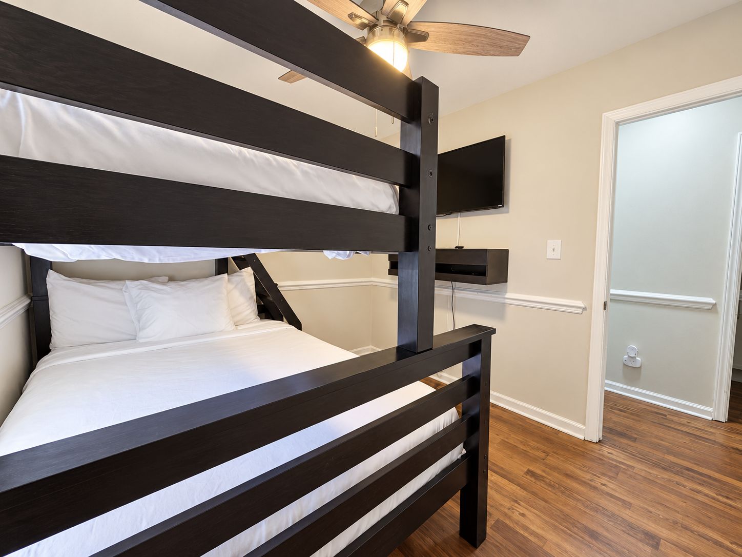 A bunk bed with a ceiling fan, a mounted TV, and a door leading to another room.