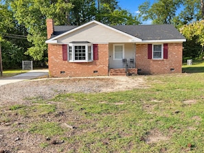 A single-story brick house with a front porch, a garage, and a small front yard. - Cozy 3-bedroom Rocky Mount Home Retreat With Full Kitchen & Fenced Yard (Rocky Mount)