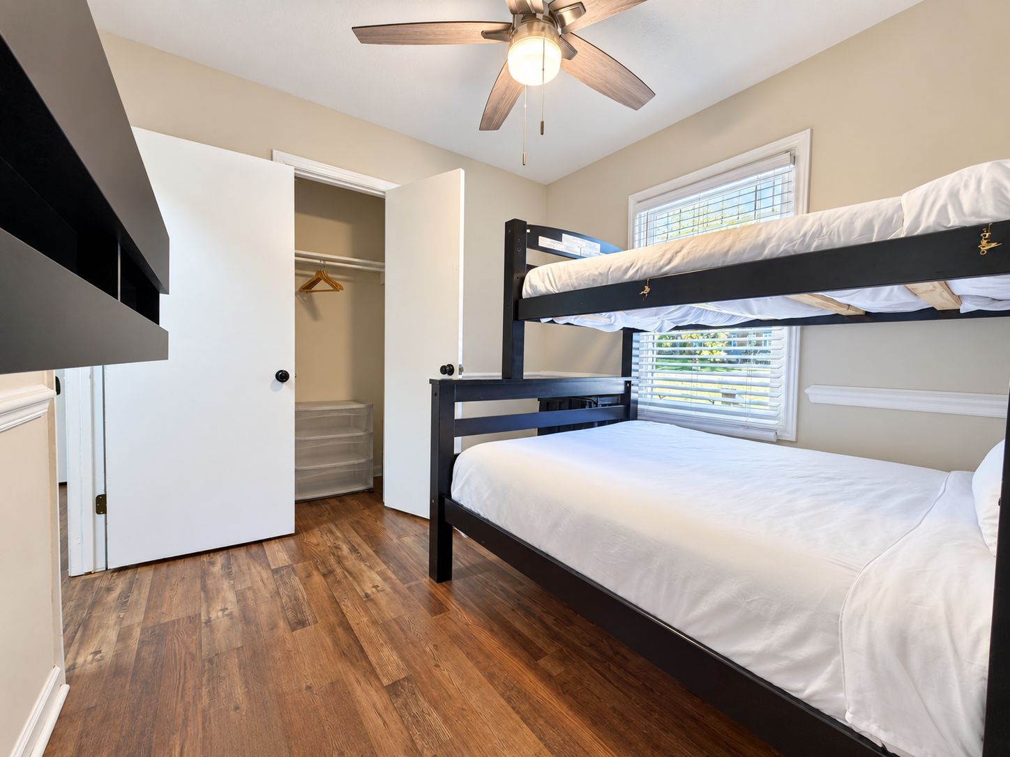 A bunk bed room with a ceiling fan, a walk-in closet, and a window with blinds.