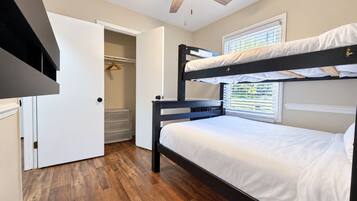 A bunk bed room with a ceiling fan, a walk-in closet, and a window with blinds.