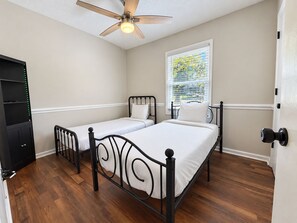 A bedroom with two single beds, a ceiling fan, a window with blinds, and a door with a lock. - Cozy 3-bedroom Rocky Mount Home Retreat With Full Kitchen & Fenced Yard (Rocky Mount)