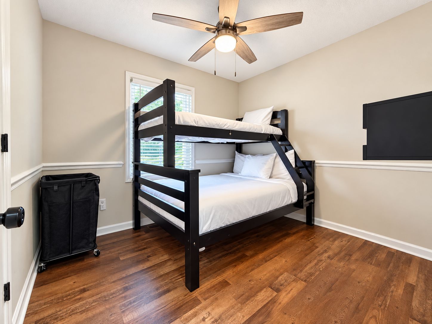 A bunk bed room with a ceiling fan, a window with blinds, and a black bag on the floor.