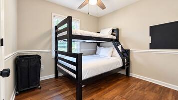 A bunk bed room with a ceiling fan, a window with blinds, and a black bag on the floor.