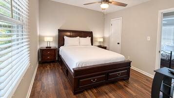 Un dormitorio con una cama de madera, un ventilador de techo y una mesita de noche con una lámpara.