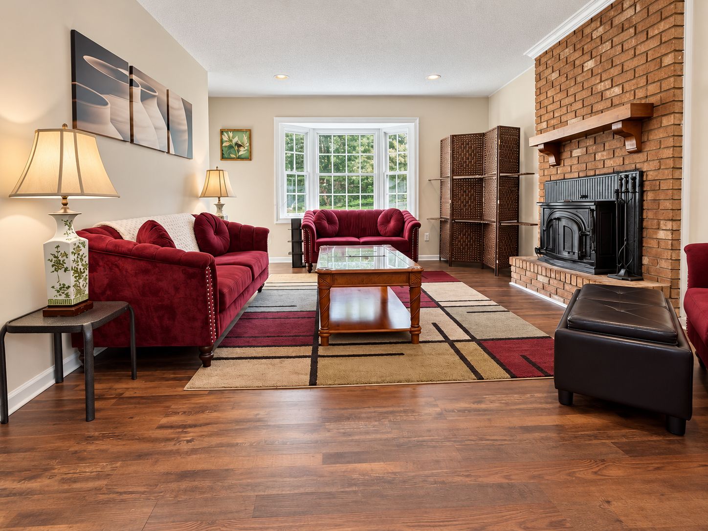A living room with a fireplace, red sofas, a glass coffee table, and a brick wall.
