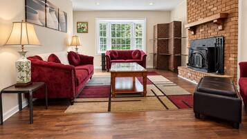 A living room with a fireplace, red sofas, a glass coffee table, and a brick wall.