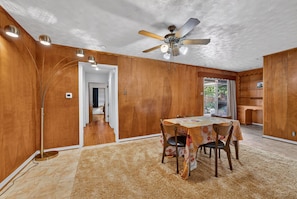 A room with a dining table, chairs, a ceiling fan, and a large window. - White Rock Lake House (Dallas)
