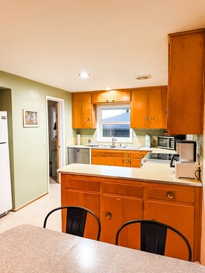 A compact kitchen with wooden cabinets, a built-in microwave, and a window above the sink. - Cozy midcentury home in South Eugene - 1 mi. to UO + walkable to cafes & trails (Eugene)