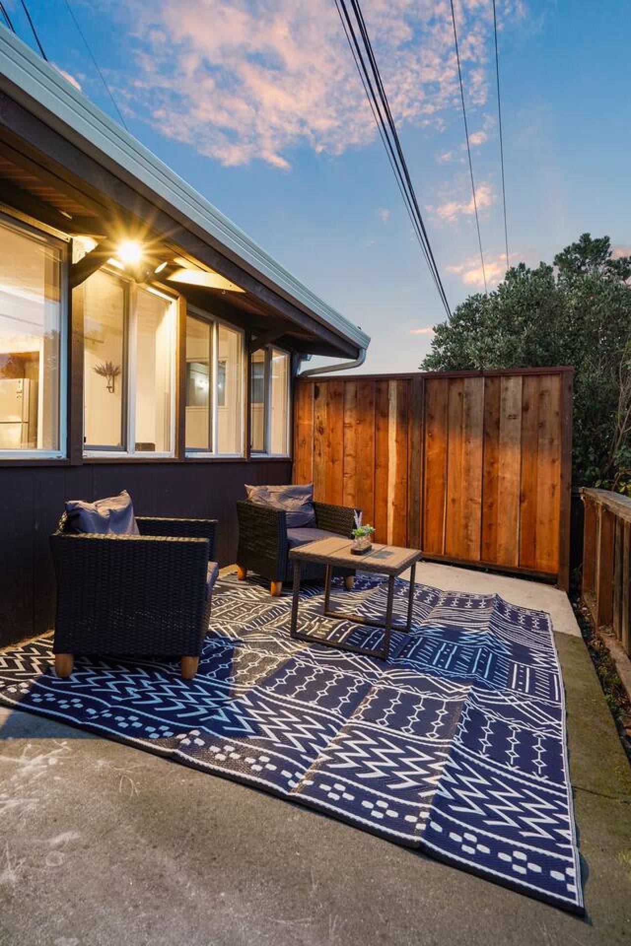 An outdoor patio with a dark-colored sofa, a small table, and a patterned rug.