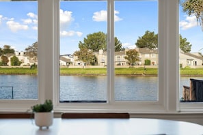 Vista a través de una ventana que muestra un lago, casas y una zona con césped.