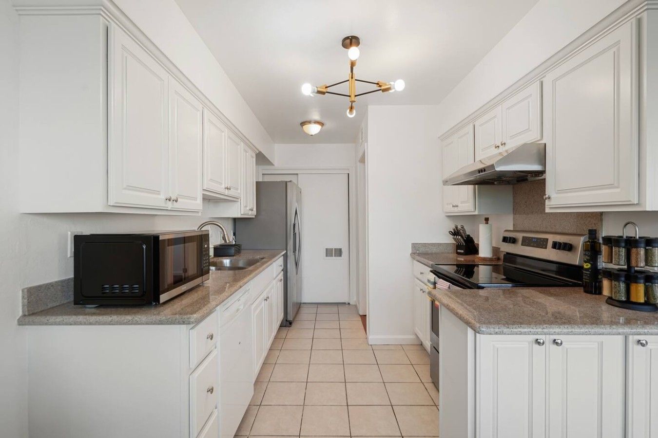 A modern kitchen with white cabinetry, a black microwave, a stainless steel refrigerator, and a gas stove.