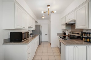 Een moderne keuken met witte kasten, een zwarte magnetron, een roestvrijstalen koelkast en een gasfornuis.