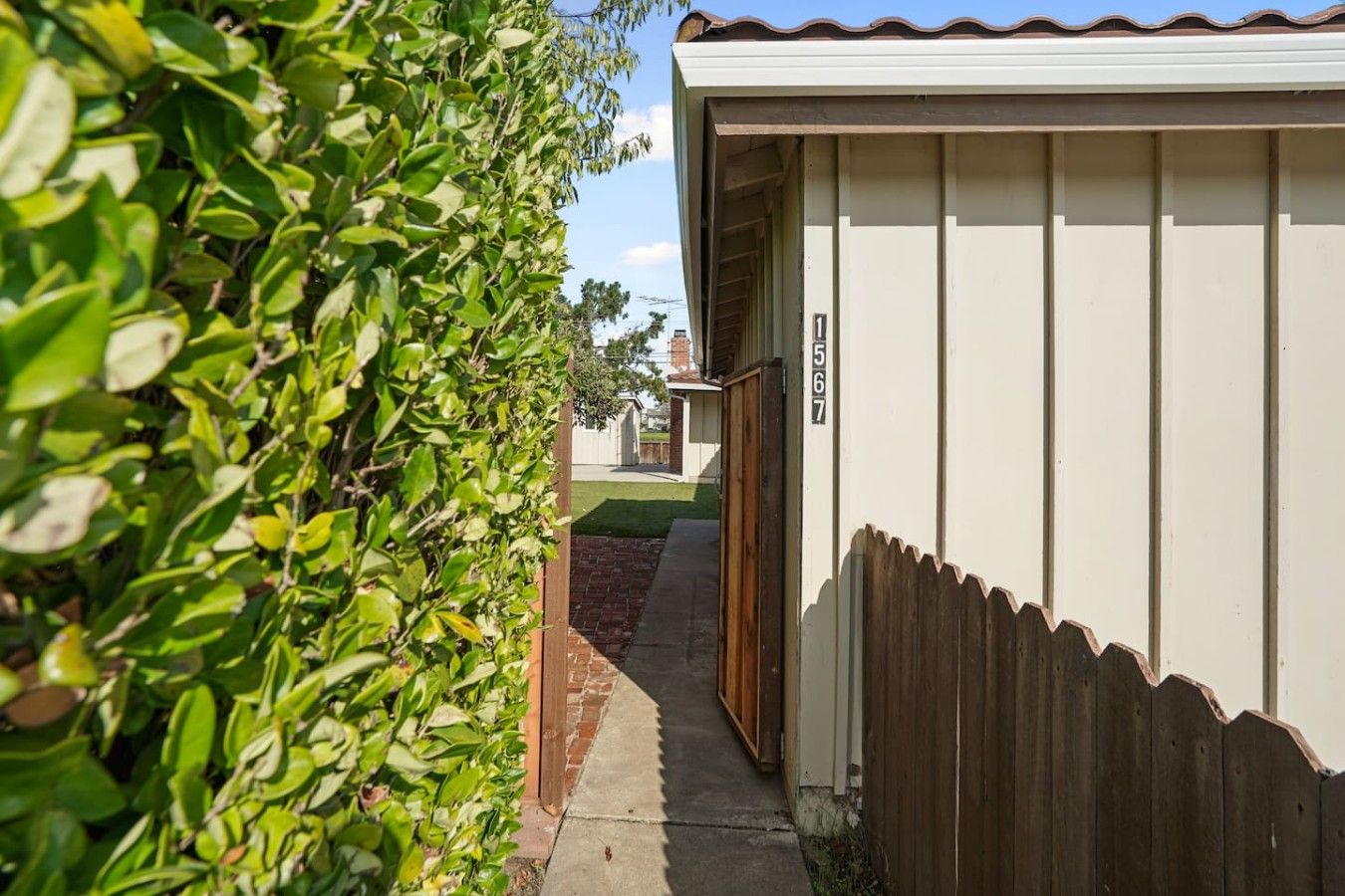 A narrow pathway leading to a building with a wooden fence and a number sign.