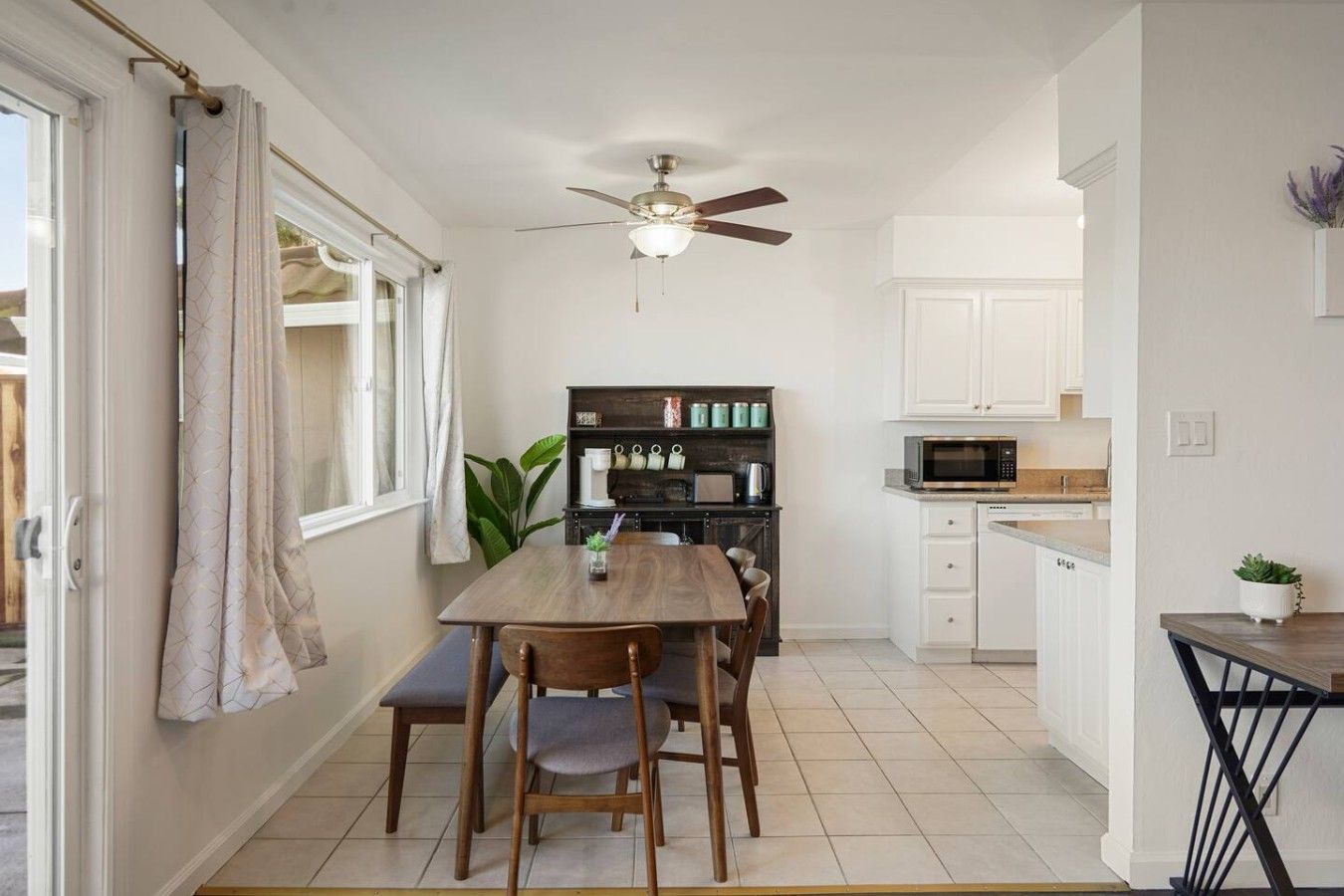 A compact kitchen with a dining area, a ceiling fan, and a window with curtains.