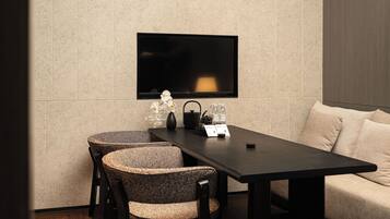 A modern dining area with a flat-screen TV mounted on the wall, a dark wooden table, two woven chairs, and a pendant light.