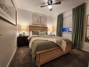 Ein Schlafzimmer mit einem hölzernen Bett, zwei Nachttischlampen, einem Deckenventilator und einem Fenster mit Vorhängen.