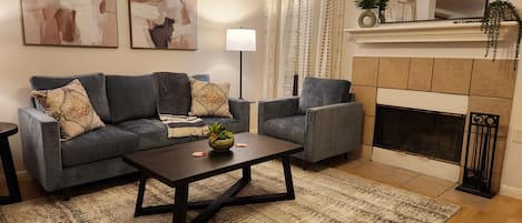 A living room with a sofa set, a coffee table, a fireplace, and abstract wall art.