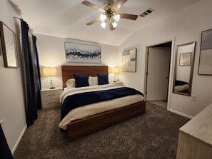 Une chambre à coucher avec un lit, des lampes de chevet, un ventilateur de plafond et des œuvres d’art accrochées aux murs.