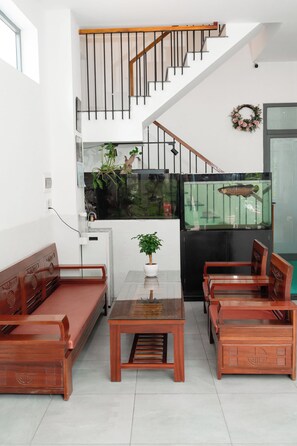 A modern living room with a glass coffee table, wooden sofas, a staircase with a wooden handrail, and a fish tank. - Green Apartment (An Hai)