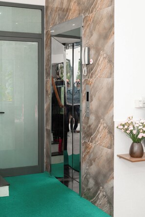 An elevator with a glass door, a marble wall, and a green carpeted floor. - Green Apartment (An Hai)