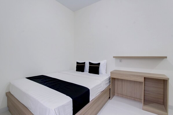 A single bed with a white mattress and black bedding, a bedside table, and a wooden nightstand.