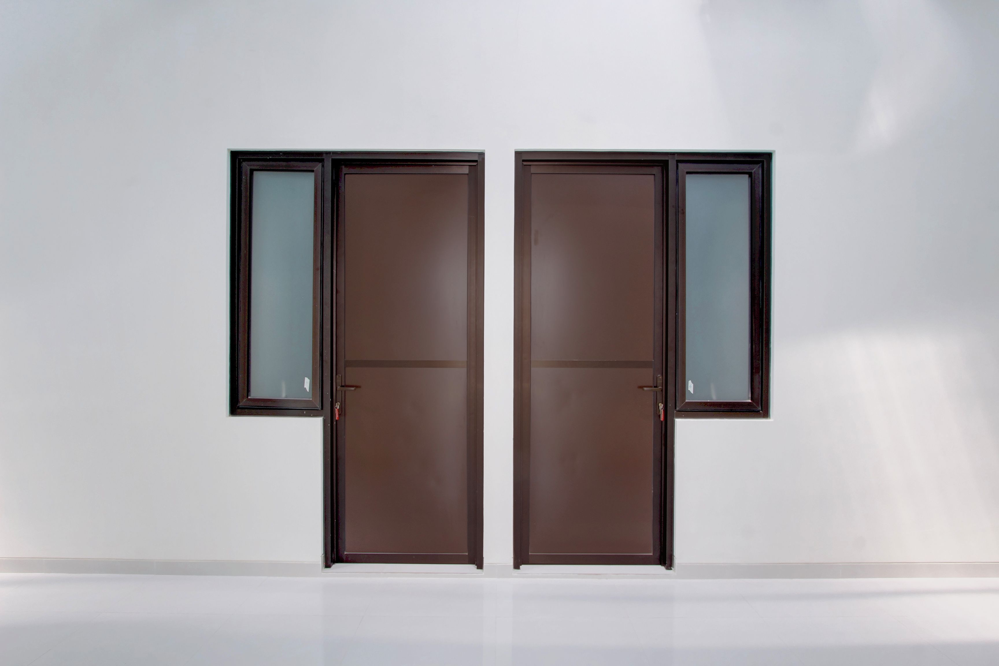 A pair of double doors with a frosted glass panel, set in a plain white wall with a reflective floor.