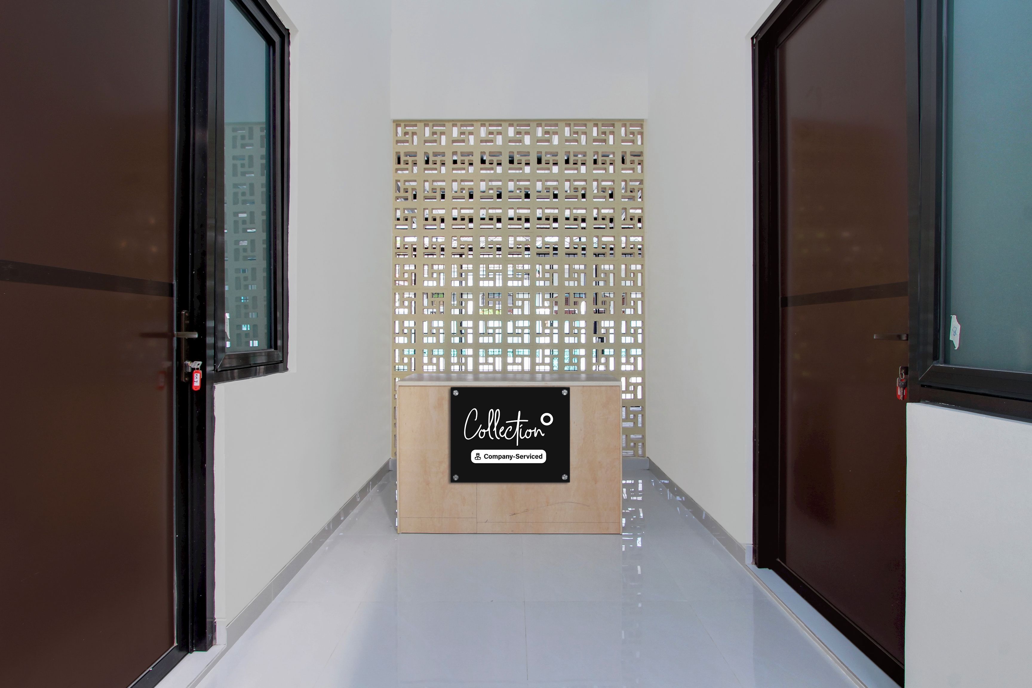 Un pasillo con dos puertas a cada lado, un panel decorativo con un letrero que indica un área de recolección de servicios de la empresa, y piso de baldosas.