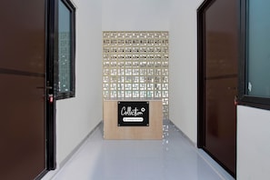 Un pasillo con dos puertas a cada lado, un panel decorativo con un letrero que indica un área de recolección de servicios de la empresa, y piso de baldosas.