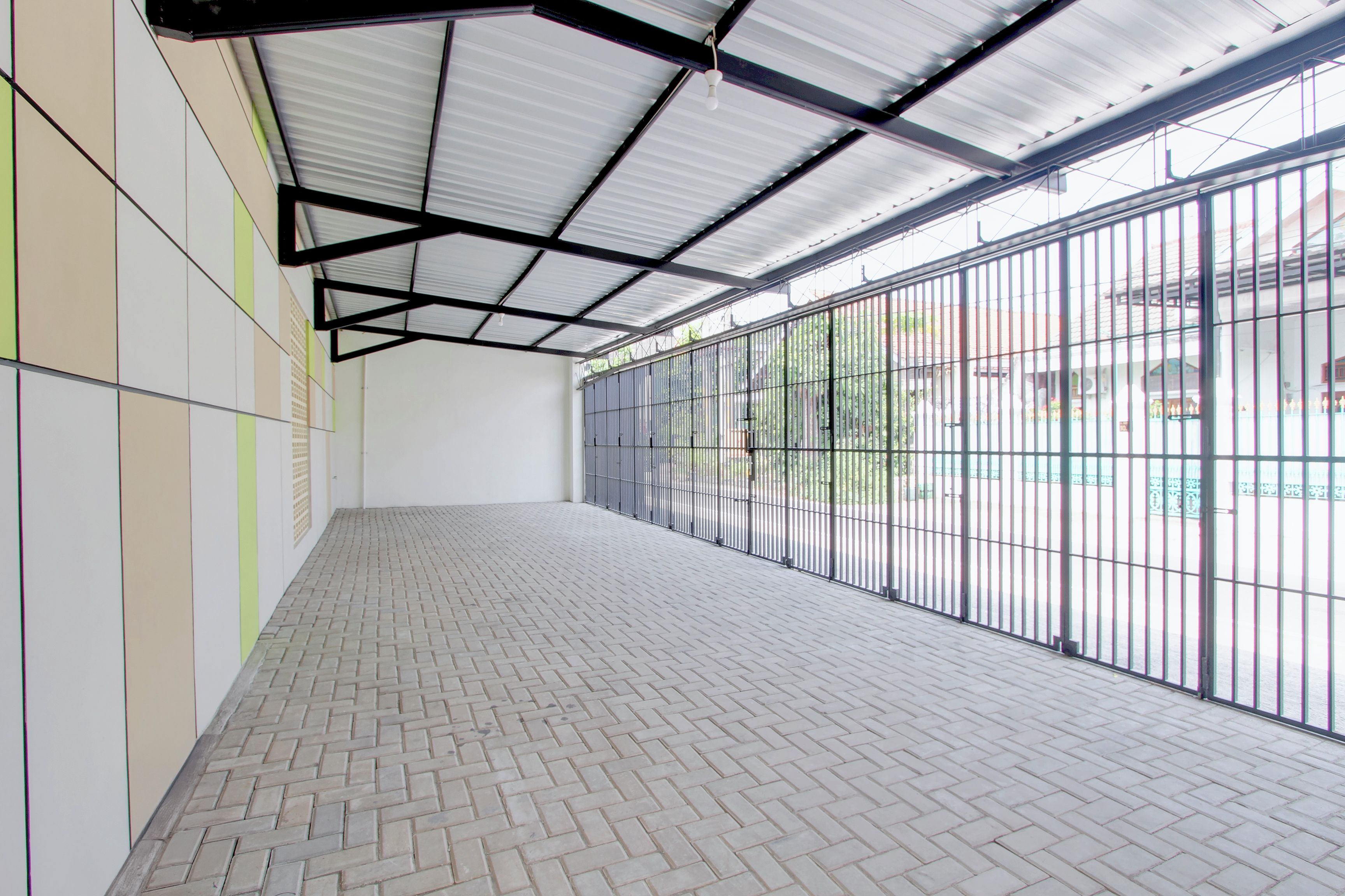 Un espacio interior amplio con piso de baldosas, techo de estructura metálica y un ventanal con barrotes.