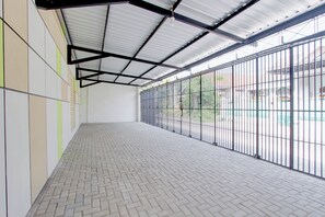 Un espacio interior amplio con piso de baldosas, techo de estructura metálica y un ventanal con barrotes.