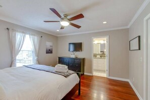 A bedroom with a bed, a dresser, a ceiling fan, a television, and a bathroom visible through an open door. - Stylish Getaway Prime Location Near Downtown (Nashville)