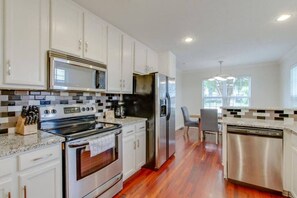 A modern kitchen with white cabinets, stainless steel appliances, and a wooden floor. - Stylish Getaway Prime Location Near Downtown (Nashville)