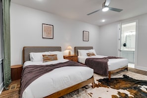 Ein Hotelzimmer mit zwei Betten, einem Deckenventilator, einem Nachttisch mit Lampe und einem Kuhfellteppich.
