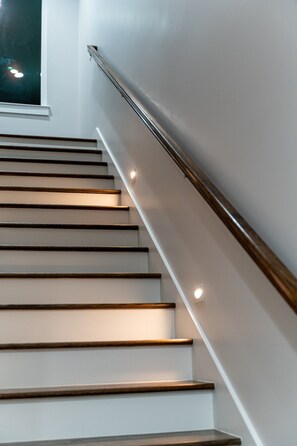 A staircase with wooden steps and a metal handrail, leading to a landing with a window. - Triple Townhome Combo | Skyline Decks (Nashville)
