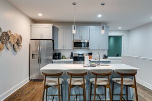 A modern kitchen with white cabinets, stainless steel appliances, and a central island with bar stools. - Triple Townhome Combo | Skyline Decks (Nashville)