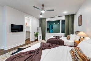 A hotel room with two beds, a ceiling fan, a TV, a window with curtains, and a plant. - Triple Townhome Combo | Skyline Decks (Nashville)