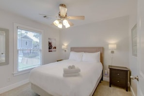 Un dormitorio con cama, mesita de noche, ventilador de techo y ventana con persianas.