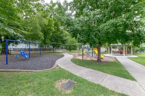 A playground with a blue swing set and a yellow slide, surrounded by trees and a paved walkway. - Two Modern Home Retreat Near Downtown! Sleeps 18! (Nashville)