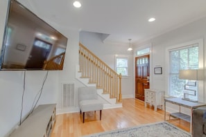 A modern interior with a staircase, a flat-screen TV mounted on the wall, a desk with a lamp, and a window with blinds. - Two Modern Home Retreat Near Downtown! Sleeps 18! (Nashville)